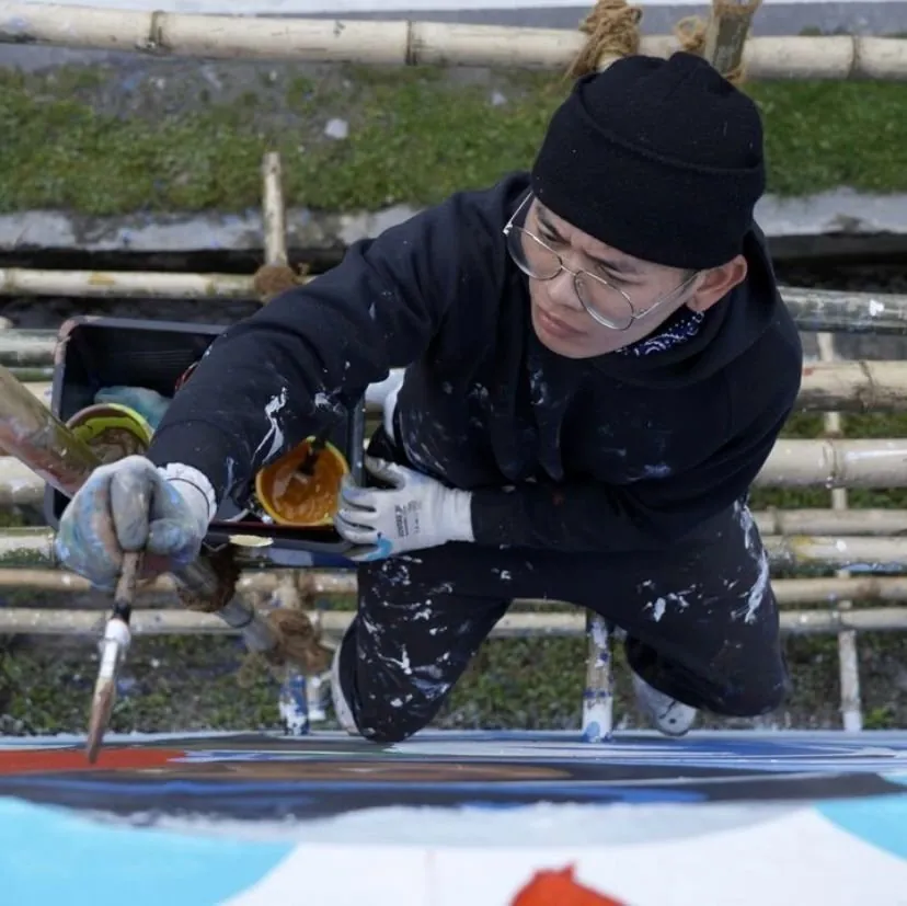 Lobsang Soepa, seen from above, painting a mural in paint-spattered clothes